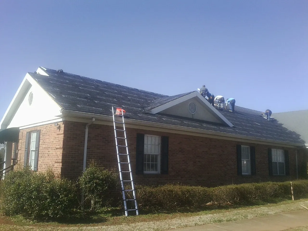 Crew tearing shingles off a brick ranch roof with a ladder set — Emergency Roof Repair work by our crew in Moss Landing