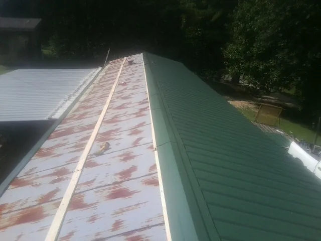 Old rusted panels beside newly installed green metal roofing — Wind Damage Roof Repair by Roofing Brothers in Moss Landing