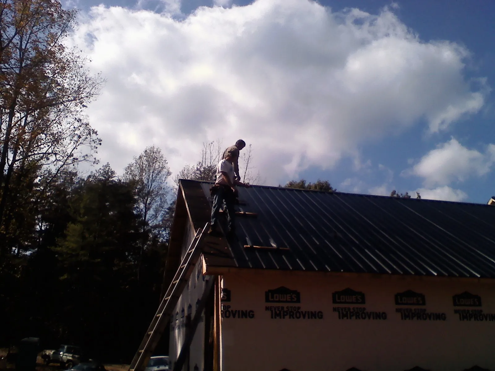 Roofer fastening dark metal panels high against a cloudy sky, from a Roof Inspection job in Moss Landing