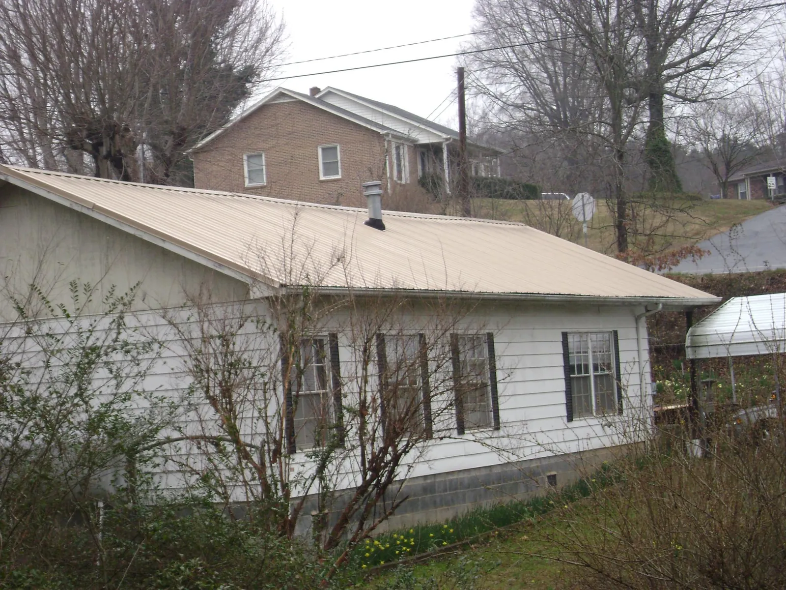 Tan metal roof on a white sided house set into a hillside — Commercial Roofing by Roofing Brothers in Moss Landing